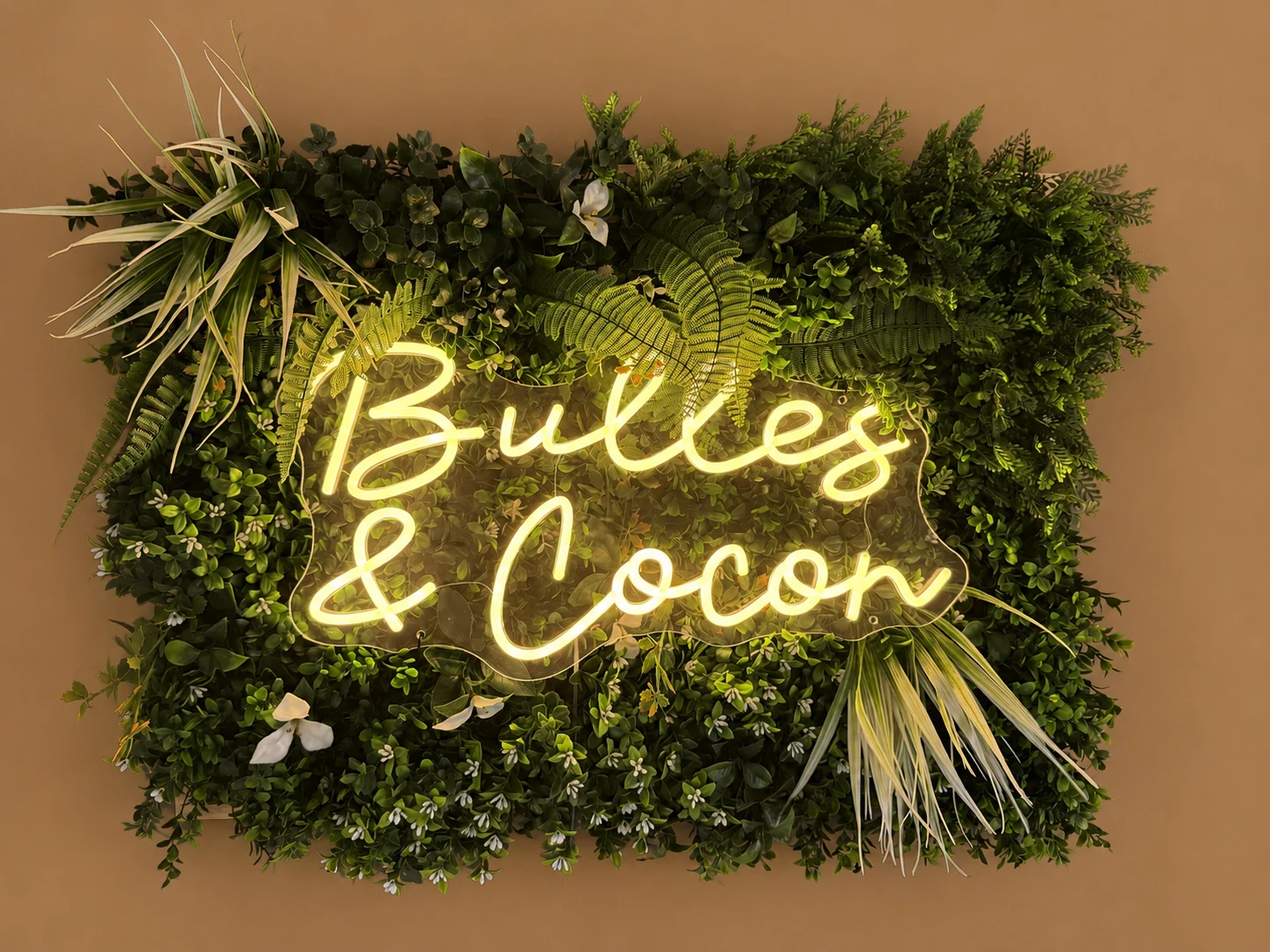 Enseigne néon Bulles et Cocon sur mur de verdure