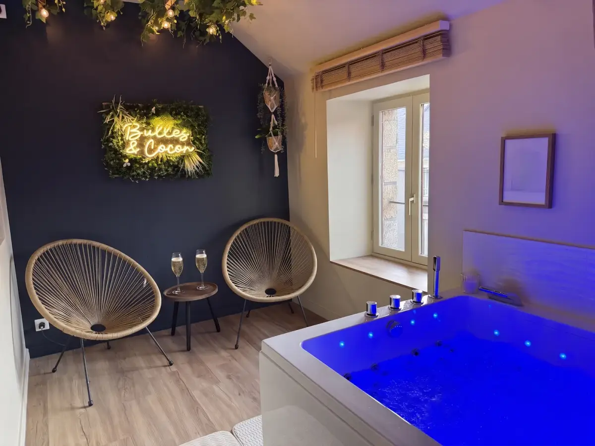 Espace spa : bain à remous, fauteuils acapulco en rotin, coupes de champagne et enseigne néon Bulles et Cocon sur mur végétal — Bulle Rochoise, Bulles et Cocon
