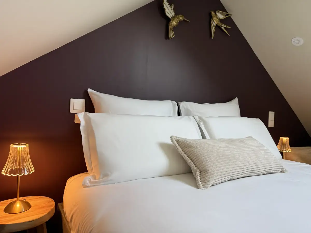 Lit douillet aux draps blancs et traversin, oiseaux dorés au mur et lampes de chevet — Bulle Rochoise, Bulles et Cocon