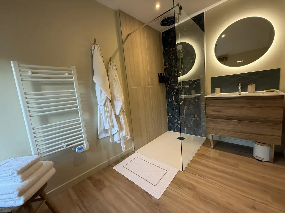 Salle d'eau : douche à l'italienne, mur floral, miroir rond lumineux et peignoirs — Bulle Rochoise, Bulles et Cocon
